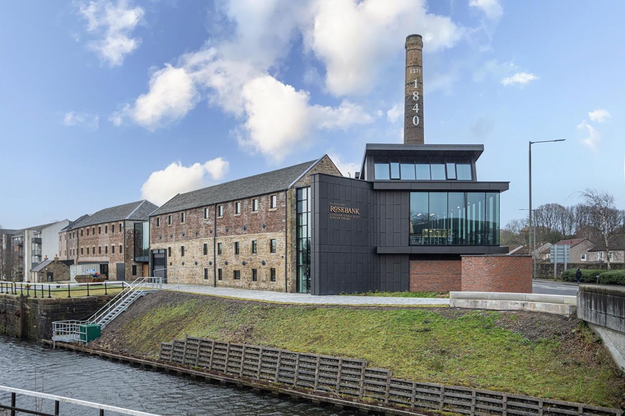 Canalside view of Rosebank Distillery Victorian brick buildings and glass fronted stillroom to the right with chimney behind